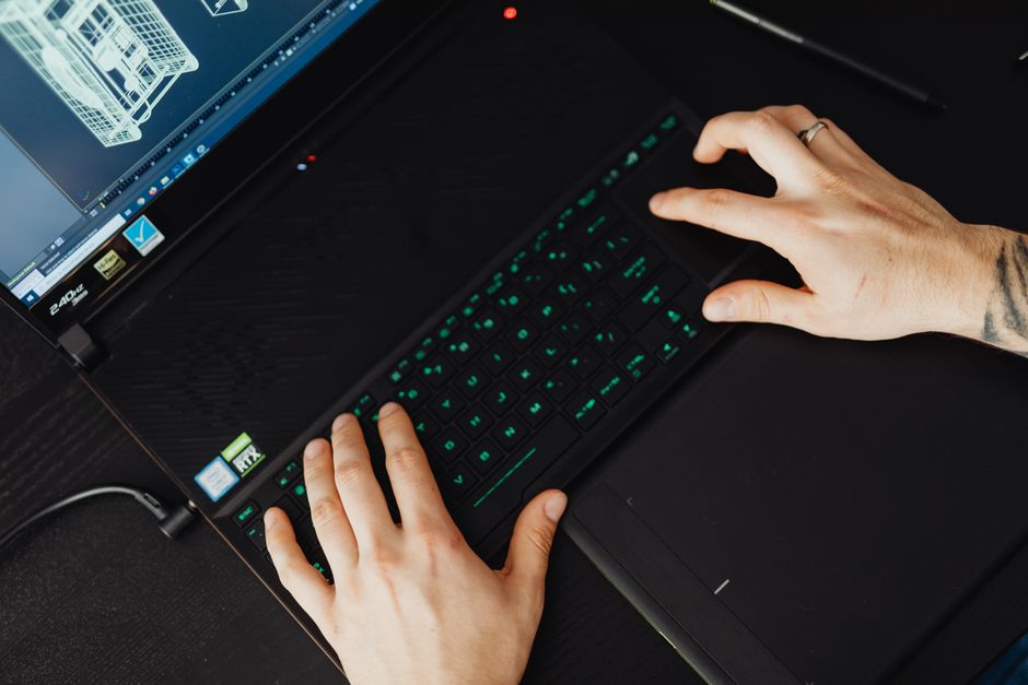 A close-up of hands typing on a laptop with blueprints and a model of a modern building on the desk, symbolizing the intersection of real estate and technology.